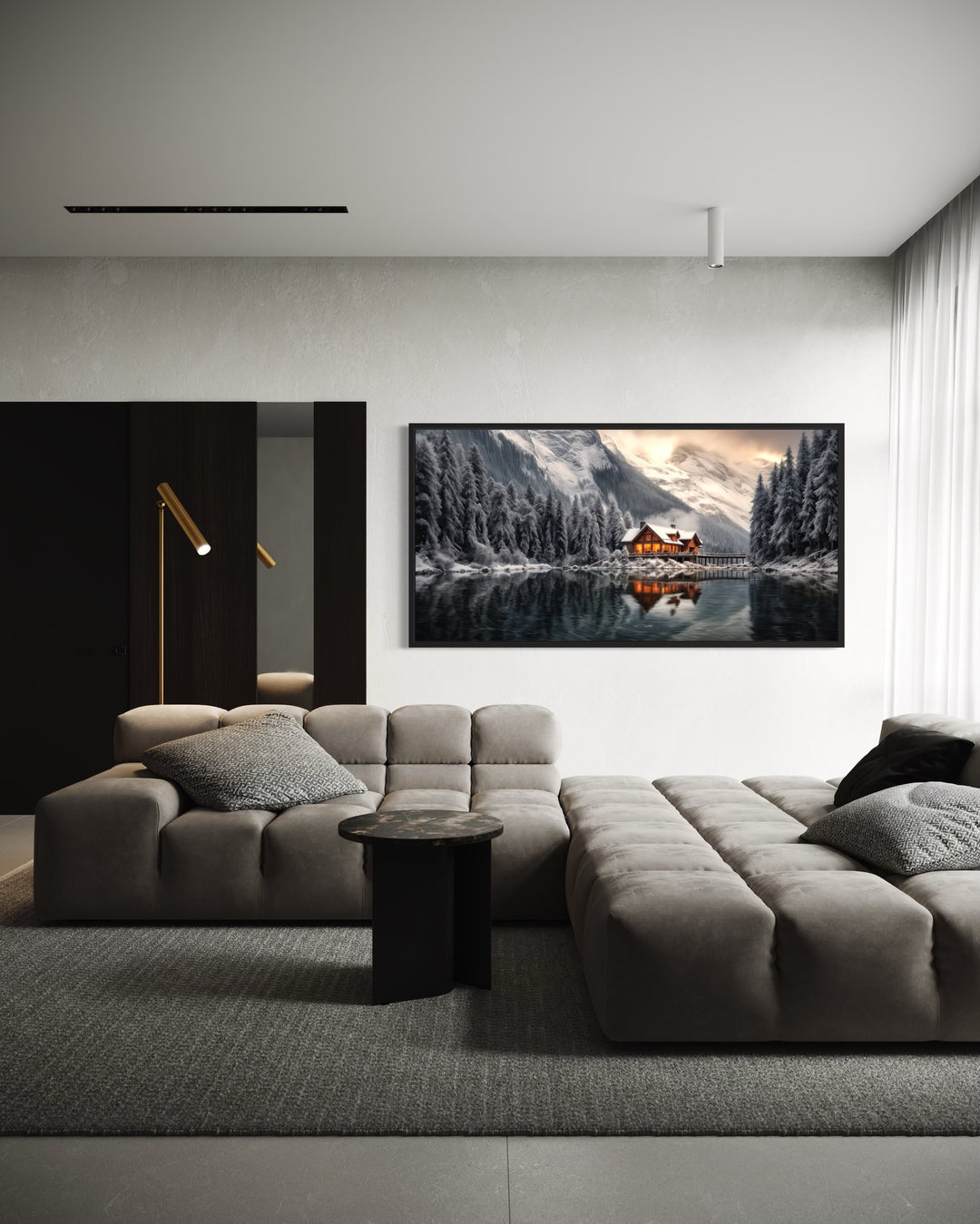 Framed panoramic canvas of a cozy winter cabin by a lake, hung above a modern grey sectional sofa.