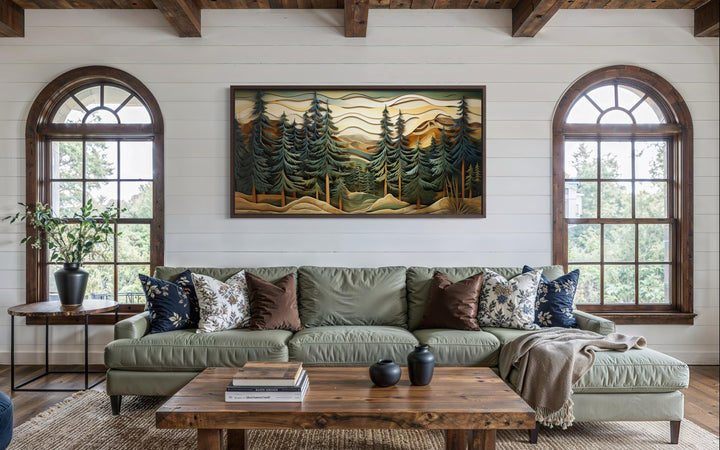 Panoramic mountain forest canvas wall art with pine trees hangs above a green sofa in a rustic room.