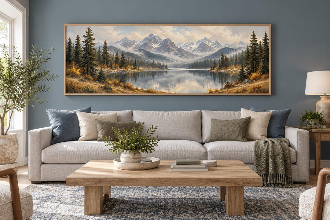 Long horizontal canvas wall art of a mountain lake and autumn forest above a living room sofa.
