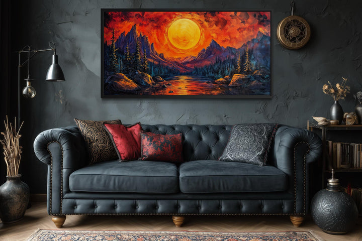 Mountain Lake Fiery Sunset canvas wall art displayed above a dark tufted sofa in a moody room.