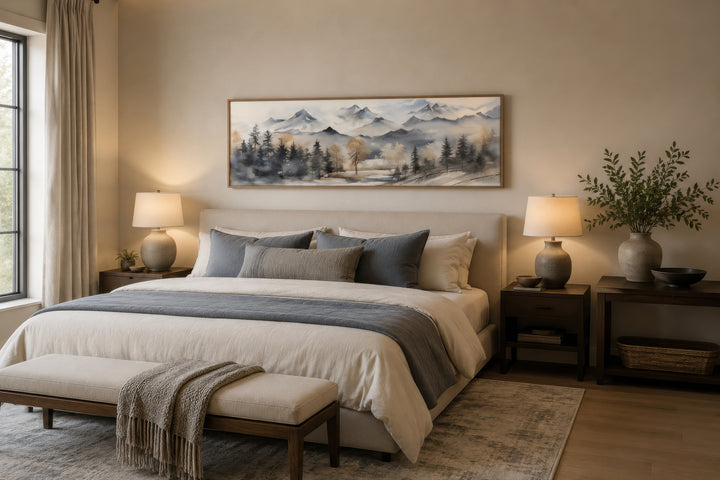Horizontal framed canvas wall art of a watercolor mountain landscape in earth tones over a bed.