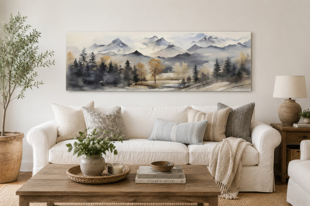 Horizontal framed canvas wall art of a watercolor mountain landscape in earth tones above a sofa.