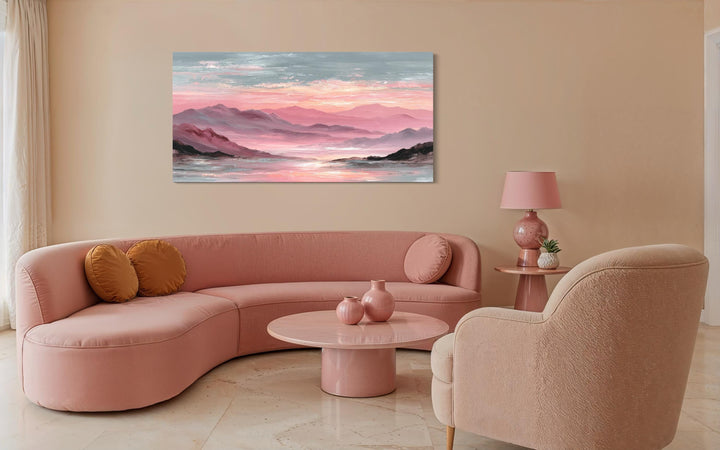 A wide canvas print of a pink mountain landscape hangs above a curved blush sofa in a modern room.