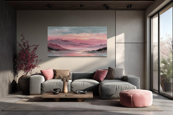 A wide canvas print of a pink mountain landscape hangs above a modern grey sofa in a minimalist room.