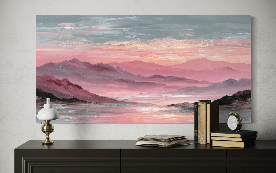 A horizontal canvas print of a pink mountain landscape at sunset hangs above a dark wooden dresser.