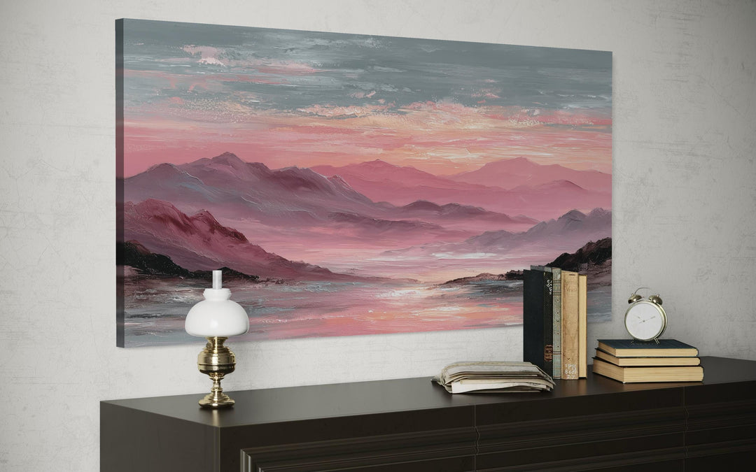 A horizontal canvas print of a pink mountain landscape at sunset hangs above a dark wooden dresser.