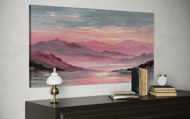 A horizontal canvas print of a pink mountain landscape at sunset hangs above a dark wooden dresser.