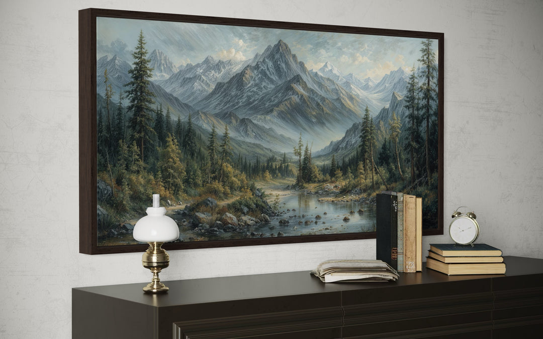 Mountain river landscape framed canvas art in an antique style, hanging above a dark wood console.