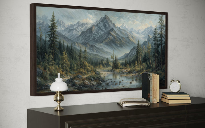 Mountain river landscape framed canvas art in an antique style, hanging above a dark wood console.