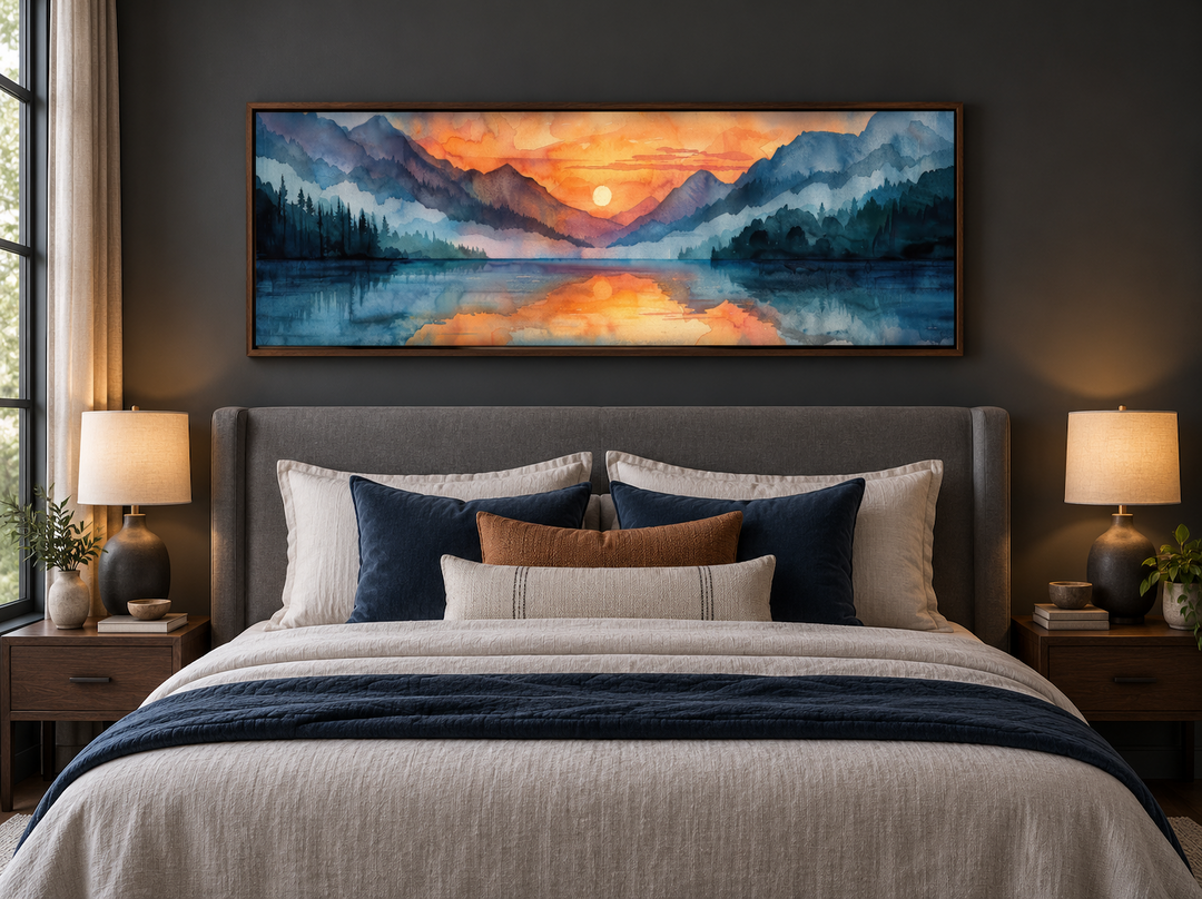 Long narrow framed canvas wall art of a watercolor mountain lake sunset above a bed.