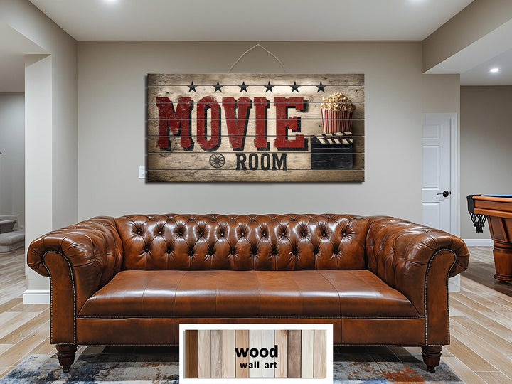 Rustic wood sign wall art with distressed red Movie Room text hanging above a brown leather sofa.