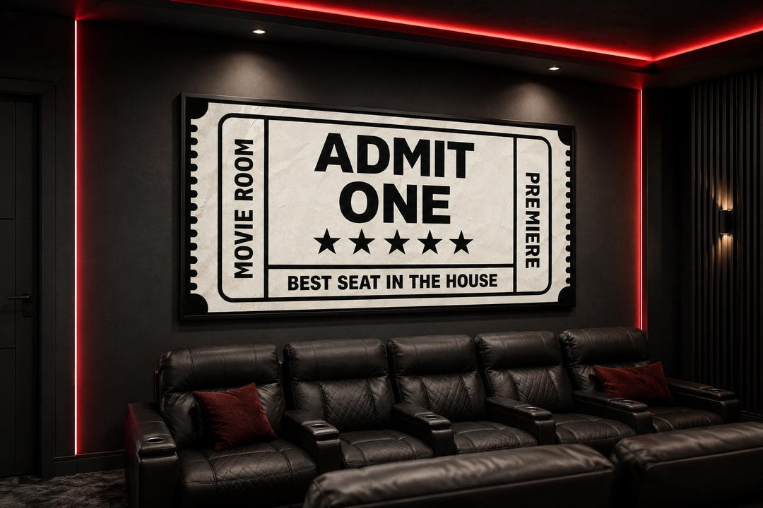 Black and beige movie ticket canvas wall art hanging in a home theater above black leather seating.