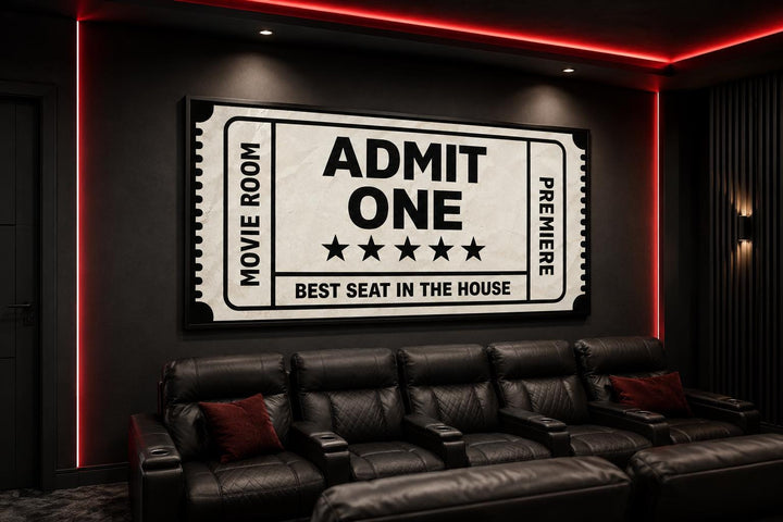 Black and beige movie ticket canvas wall art hanging in a home theater above black leather seating.