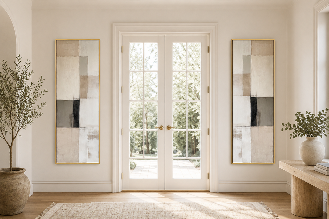 Two tall, narrow canvas prints with neutral geometric abstract blocks in gold frames on a white wall