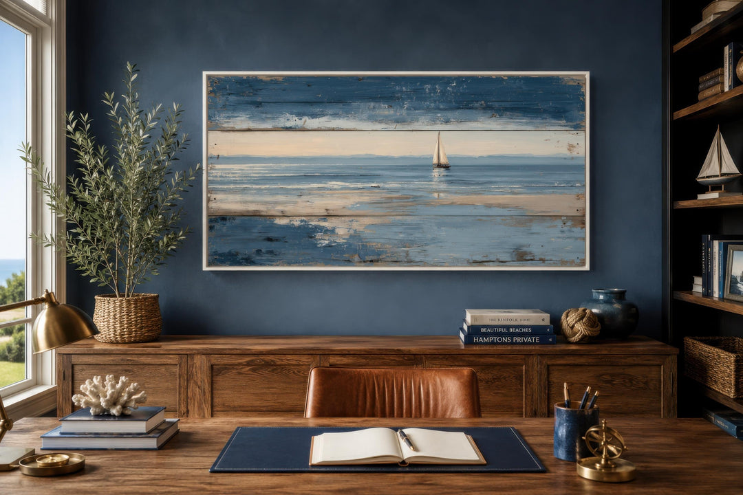 Lone sailboat canvas print with distressed wood look on a navy wall above a wooden desk.