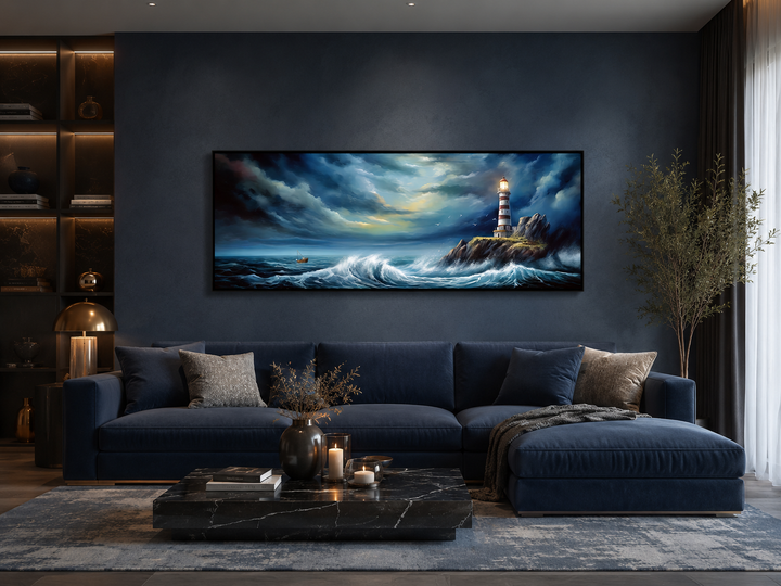 Dramatic horizontal canvas art of a lighthouse in a stormy ocean above a navy blue sofa.
