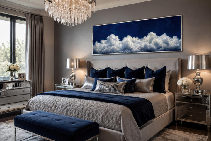 Long narrow canvas print of white clouds against a navy blue sky above a bed in a modern bedroom.