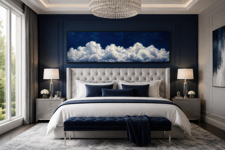 Long narrow canvas print of white clouds against a navy blue sky hanging above a tufted bed.