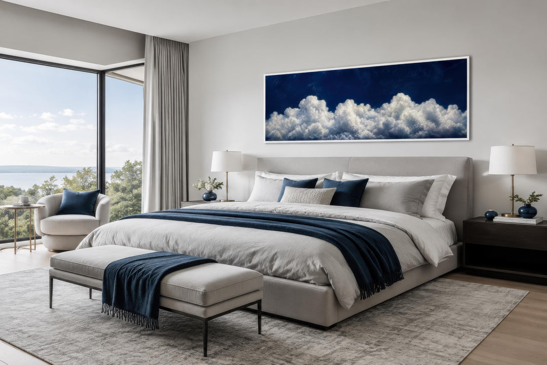 Long narrow navy blue cloud canvas print hanging above a bed in a modern neutral bedroom.