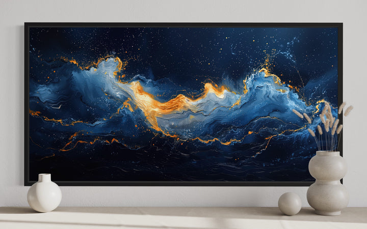 Abstract navy blue and gold ocean wave canvas wall art in a black frame above a shelf with vases.