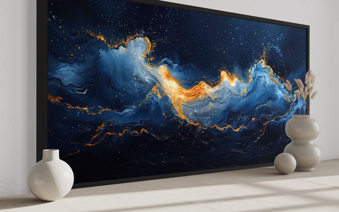 Abstract navy blue and gold ocean wave canvas wall art in a black frame on a neutral wall.