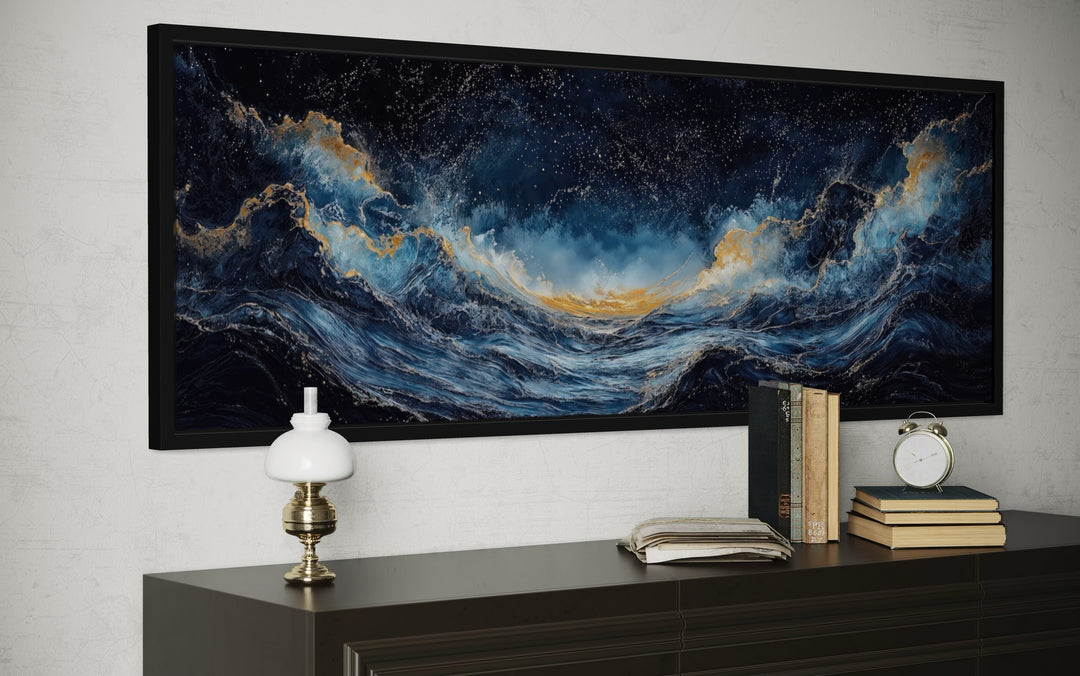 Navy blue and gold ocean wave horizontal canvas wall art in a black frame above a dark dresser.