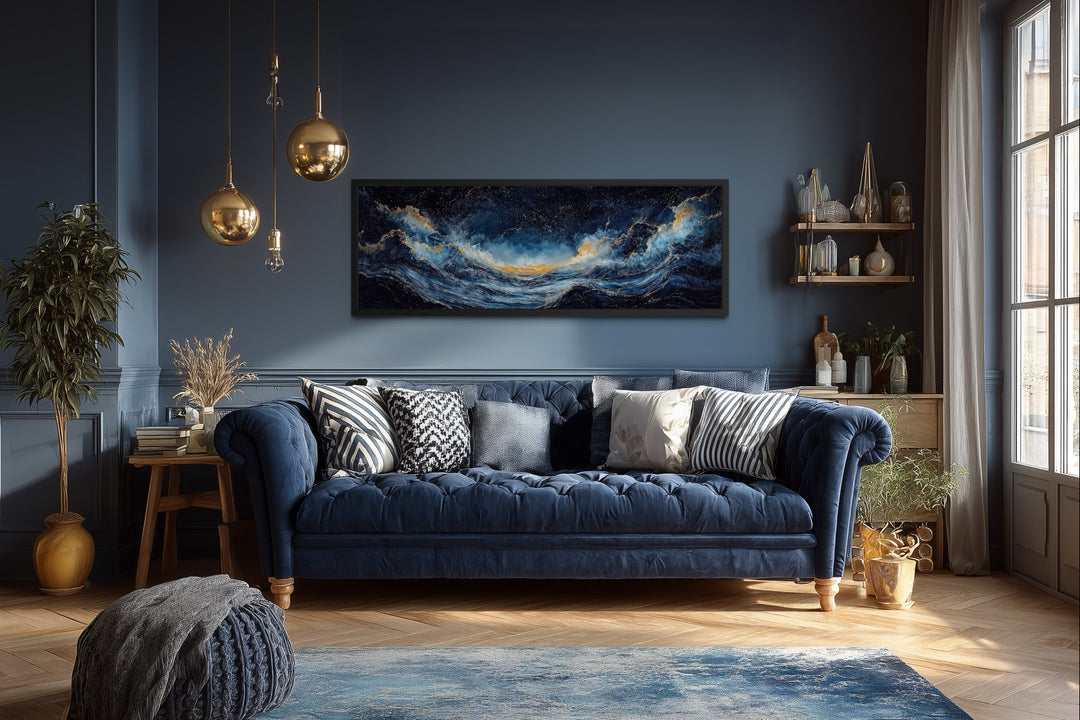 Navy blue and gold ocean wave horizontal canvas wall art framed above a blue tufted sofa.