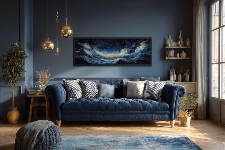 Navy blue and gold ocean wave horizontal canvas wall art framed above a blue tufted sofa.