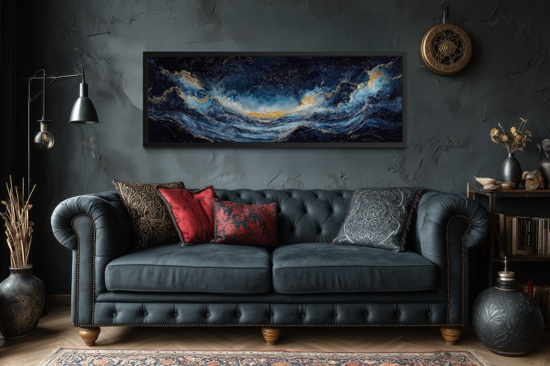 Navy blue and gold ocean wave horizontal canvas wall art hanging above a dark tufted sofa.