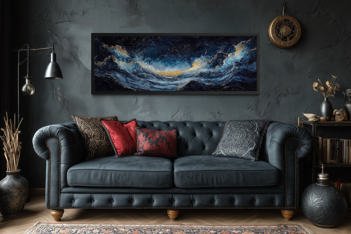 Navy blue and gold ocean wave horizontal canvas wall art hanging above a dark tufted sofa.
