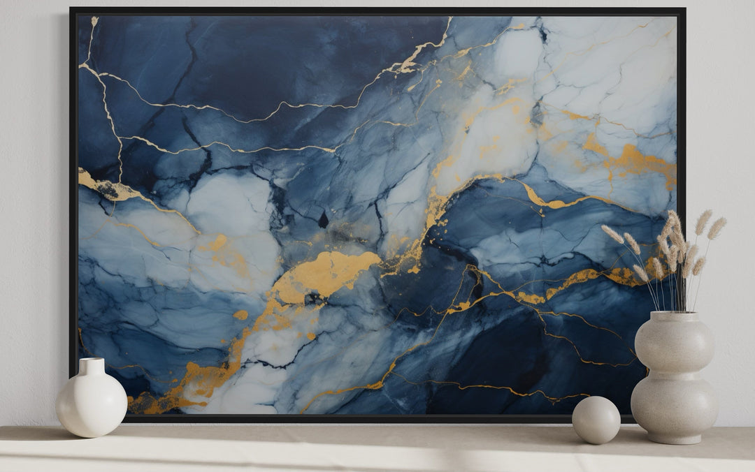 Navy blue, grey, and gold abstract marble canvas wall art in a black frame on a neutral shelf.