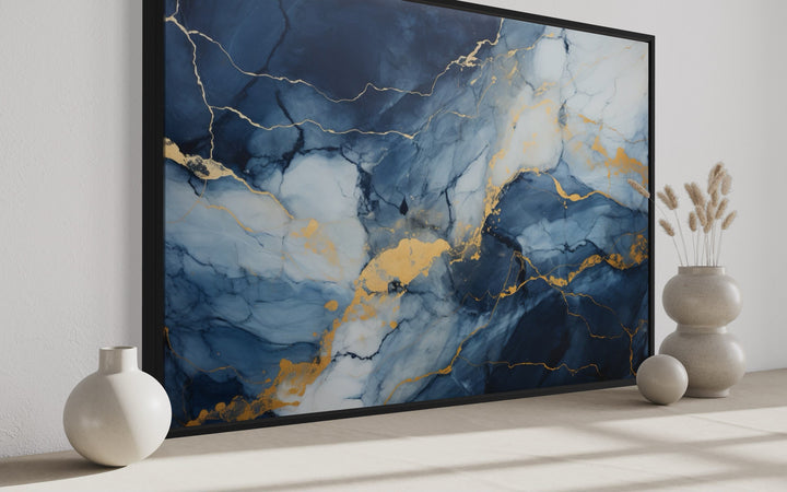 Navy blue, grey, and gold abstract marble canvas wall art in a black frame on a neutral surface.