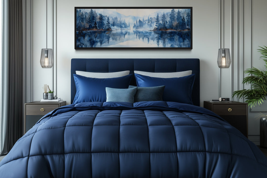 Navy blue lake landscape wall art in a black frame hanging above a bed with matching blue bedding.