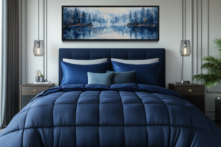 Navy blue lake landscape wall art in a black frame hanging above a bed with matching blue bedding.