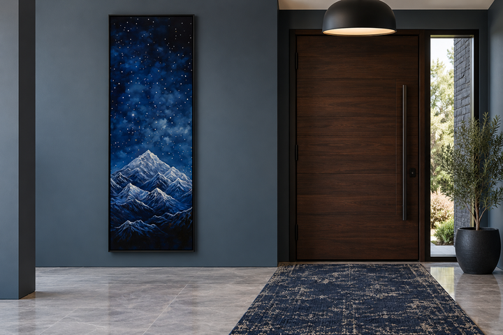 Tall narrow vertical framed canvas art of a navy blue starry night sky over snowy mountains.