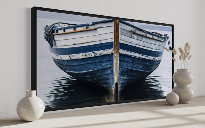 Navy blue and white old boat painting in a black frame, displayed on a wall with decorative vases.