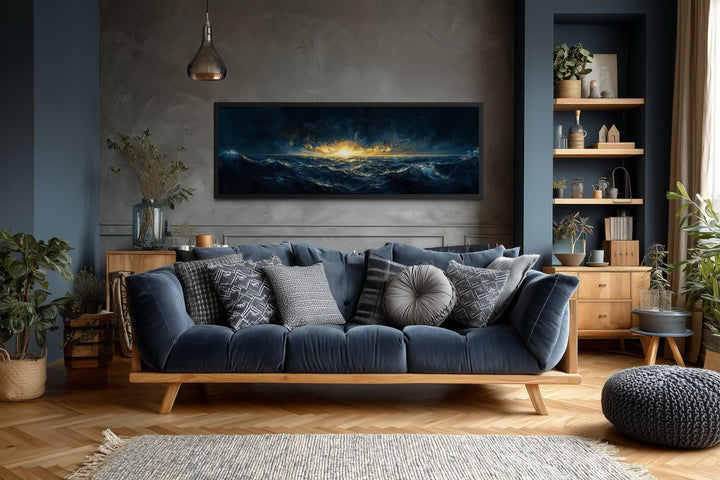 A panoramic navy and gold ocean sunset canvas hangs above a modern blue sofa in a moody living room.