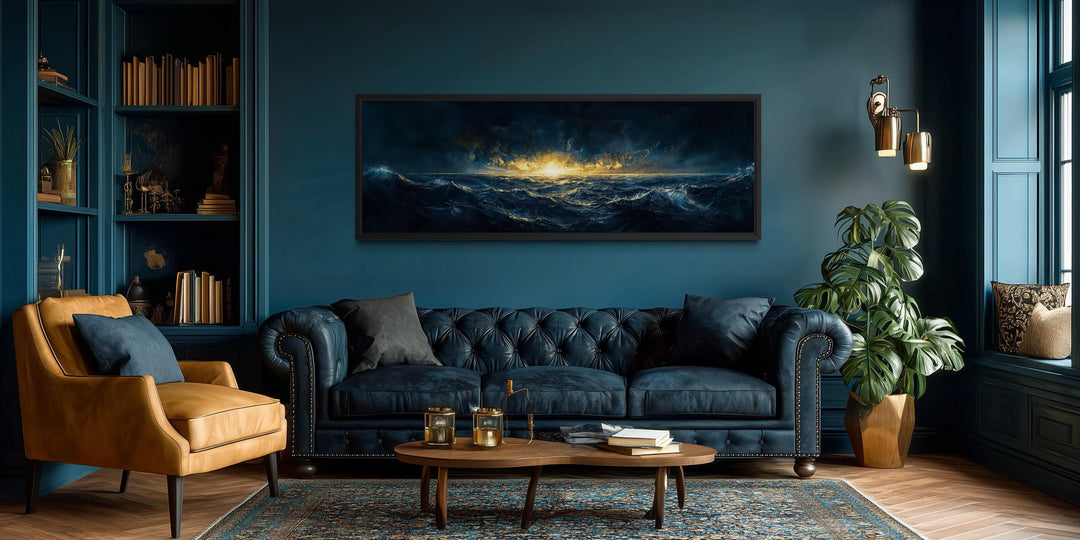 A panoramic navy and gold ocean sunset canvas hangs above a tufted leather sofa in a moody room.