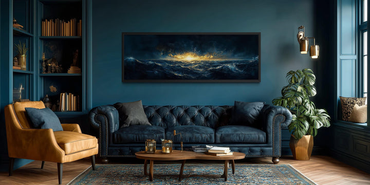 A panoramic navy and gold ocean sunset canvas hangs above a tufted leather sofa in a moody room.