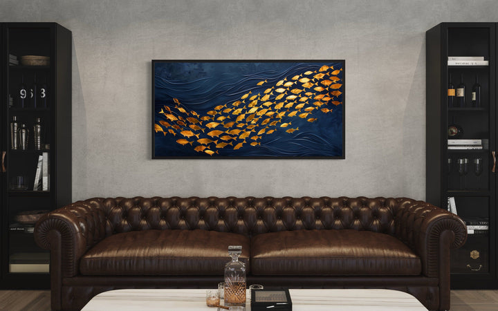 Framed navy blue canvas wall art featuring a school of shimmering gold fish above a brown sofa.