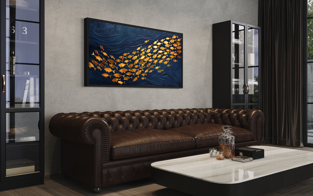 Framed navy blue canvas wall art featuring a school of shimmering gold fish above a leather sofa.