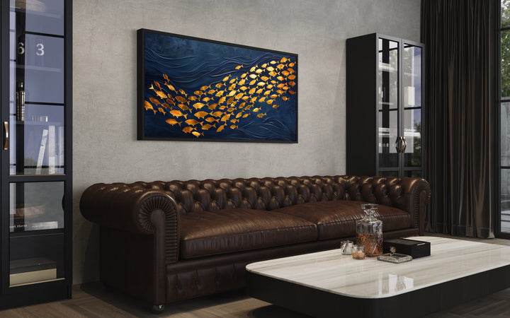 Framed navy blue canvas wall art featuring a school of shimmering gold fish above a leather sofa.