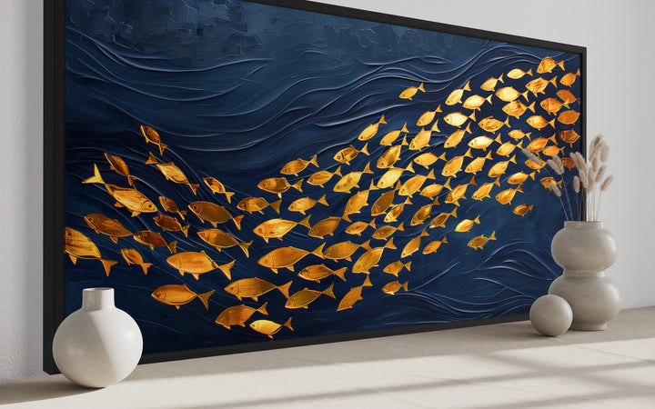 Framed navy blue canvas wall art featuring a shimmering school of gold fish in a wave pattern.