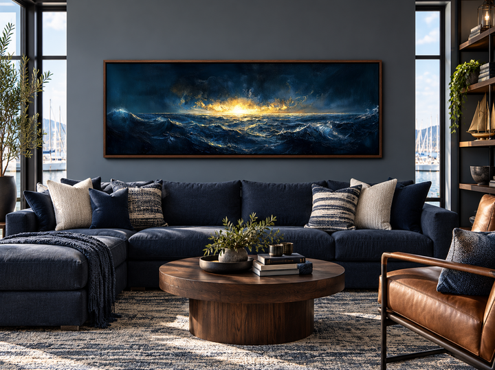 Navy and gold ocean sunset canvas art in a panoramic frame above a blue sectional sofa.