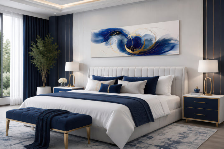 Narrow horizontal abstract canvas art with blue, white, and gold swirls hanging above a bed.