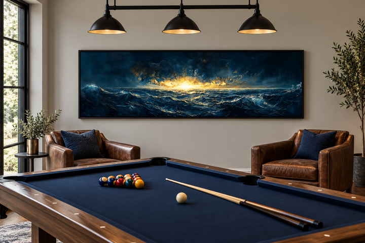 Navy and gold ocean sunset canvas art in a panoramic frame above leather chairs in a billiard room.