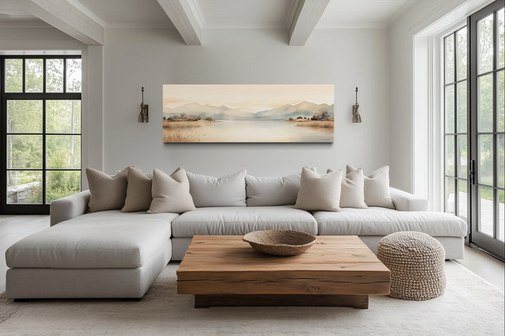 Neutral beige mountains and lake long narrow framed canvas wall art above a sofa in a living room.