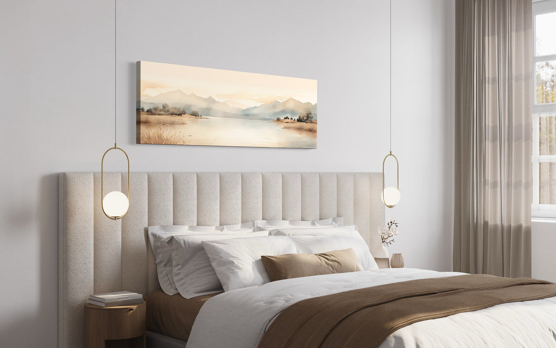 Neutral beige mountains and lake long narrow framed canvas wall art hanging above a bed.