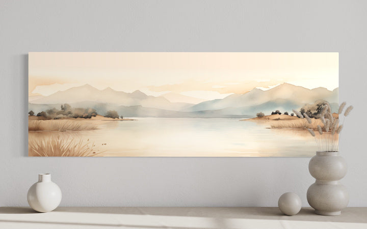 Neutral beige watercolor painting of mountains and a lake on a long narrow framed canvas.