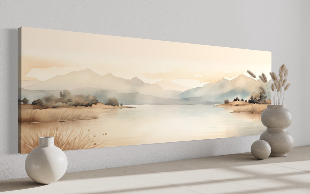 Long narrow framed canvas wall art featuring a neutral beige watercolor mountain and lake landscape.